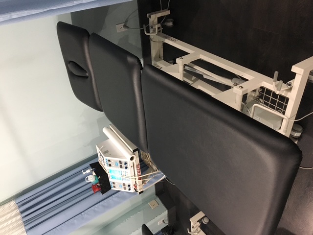 Black physiotherapy treatment table with a face opening and electrotherapy equipment in a clinic.